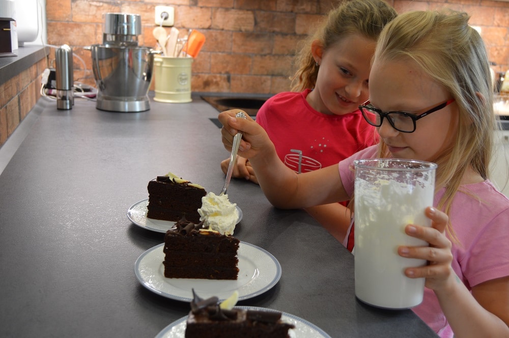 dvě mladé dívky zdobí čokoládový dort s meruňkovým džemem domácí šlehačkou