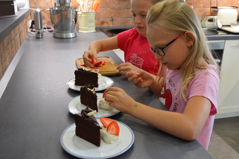 dvě mladé dívky zdobí čokoládový dort čerstvými jahodami